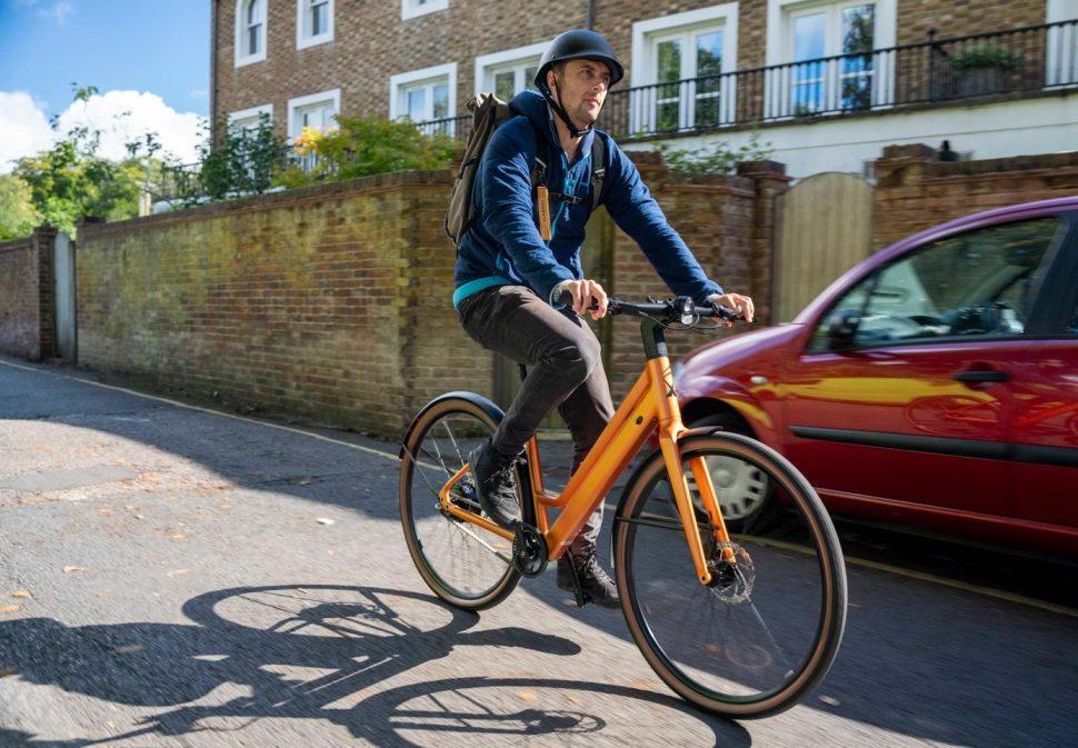 Commuter in a helmet riding an orange step-through e-bike on a residential street
