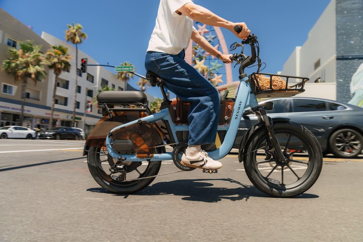 Rider on a Segway Muxi Pro cargo e-bike with front and rear baskets on a city sidewalk
